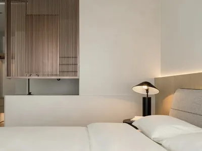 A minimalist bedroom with a white bed, wooden paneling, and modern lamp.