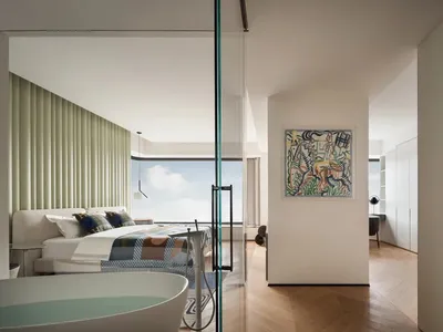 A minimalist bedroom with a large window, a queen-sized wooden bed with a patterned bedspread, and a glass bathtub.