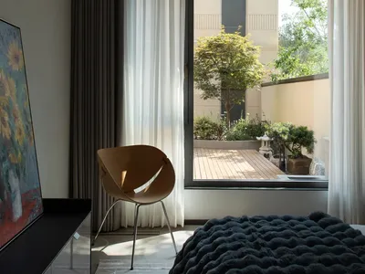 Modern bedroom with glass window overlooking outdoor terrace adorned with green plants and trees.