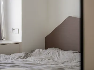 Unmade bed with grey headboard in minimalist bedroom