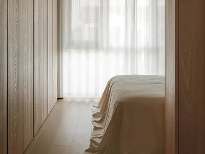 Minimalist bedroom featuring wooden shutters and glass panels, with soft lighting and neutral tones