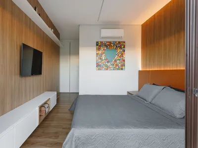 Modern minimalist bedroom featuring a bed with a wood headboard and grey bedding, a flat-screen TV on a white cabinet, and a