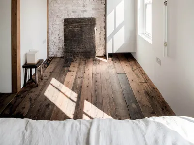 A minimalist bedroom with an angular ceiling, white brick wall, and wooden floor.