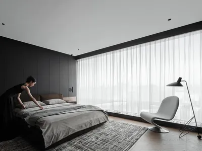 A modern minimalist bedroom featuring a bed with textured brown sheets and pillows, a gray armchair, and a floor lamp.