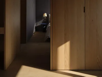 A modern, minimalist wooden doorway with a lamp in the adjacent bedroom.