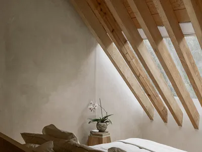 A minimalist bedroom with a wooden roof and white bedding, featuring a small white orchid on a wooden stool.