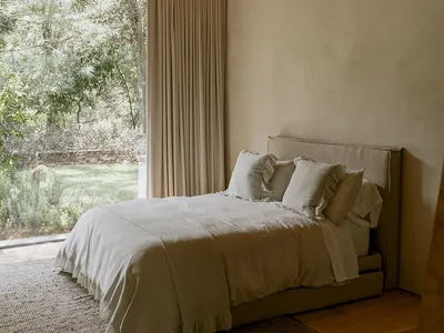 A minimalist bedroom featuring a bed with white bedding and neutral-toned walls and ceiling