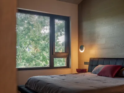 Minimalist-style bedroom featuring wooden walls and floors, with a large window overlooking greenery and a simple bed with cu
