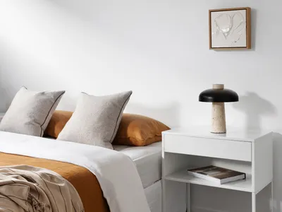 A minimalist bedroom with neutral tones furniture, including a bed with white sheets and orange throw pillows, a white nights