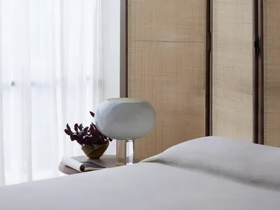 Minimalist bedroom featuring a white fabric screen behind a neatly made bed, with a clean and airy window curtain letting in