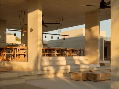 Minimalist rural hotel terrace with concrete columns, seating, and dining tables.