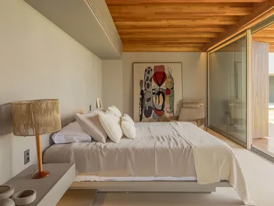 Neutral-toned modern minimalist bedroom with a wooden ceiling and a large abstract painting.
