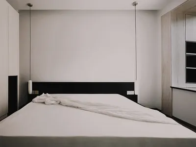極簡臥室，白色質感床罩搭配黑色床頭板，置於素淨牆面並懸掛燈具。