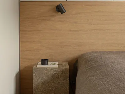A minimalist bedroom featuring a wooden headboard and a bed with a neutral-colored comforter, set against a wall with built-i