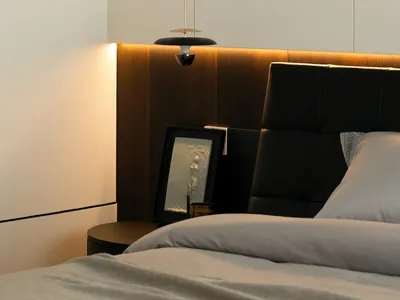 Modern minimalist bedroom featuring a wooden fabric upholstered headboard next to a white wall.