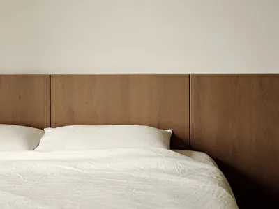 A minimalist bedroom featuring a wood headboard and white bedding.