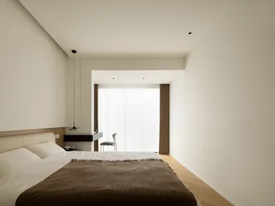 A minimalist bedroom with neutral-toned furniture, white bed linen, and a simple design.