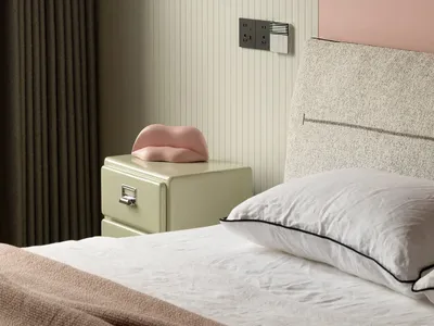 Minimalist bedroom with a patterned upholstered headboard and white bed, featuring a soft pink pillow and a green bedside dra