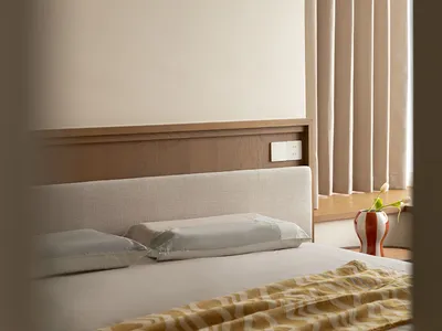 Minimalist bedroom with a bed featuring a fabric blanket, white bedding, and a wooden headboard.