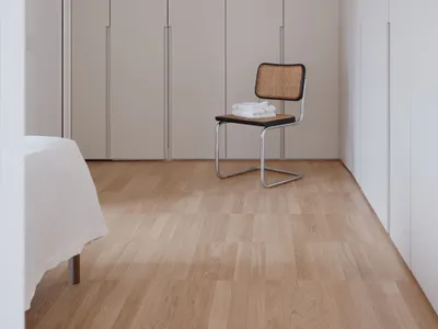 A minimalist bedroom featuring a natural wood floor and a modern chair with a cane seat, against a wall with fitted wardrobes