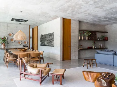 A spacious, modern industrial living room with concrete walls and floors, featuring a blue sofa and wooden furniture.