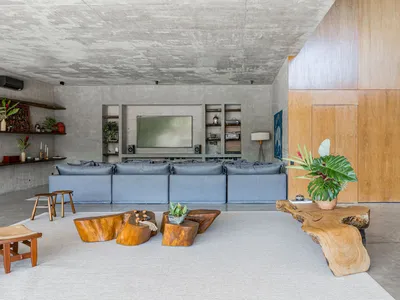 An industrial living room with concrete floors and walls, featuring a large gray sectional sofa, wooden coffee tables, and a