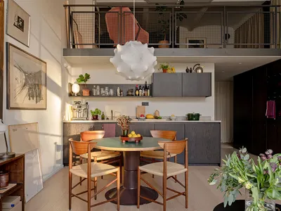 Modern kitchen with a neutral-toned wooden table, chairs, and cabinets. Features include a round dining table, pendant light,