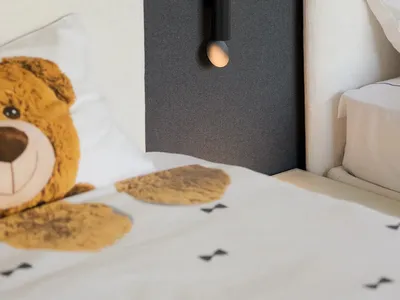 A modern minimalist bedroom featuring a fabric bed with metal headboards and a decorative teddy bear.