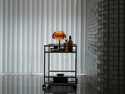 A minimalist bedroom featuring glass blinds, a concrete floor, and a brick wall.