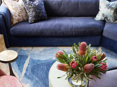 Industrially themed living room featuring a blue couch, floral arrangement, and wooden coffee table on a patterned rug.