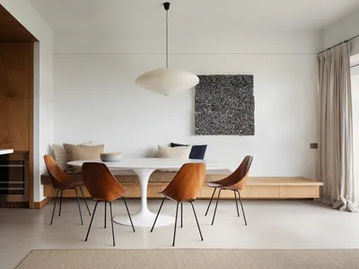 A modern Scandinavian dining room with a round table, wooden chairs, and concrete flooring.