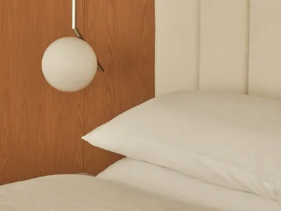 A modern minimalist bedroom featuring a wooden wardrobe and upholstered headboard with plush pillows.