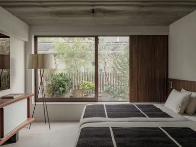 A minimalist bedroom with a large window, natural lighting, and a wooden headboard.