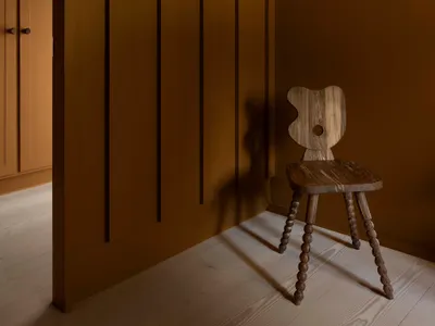 A minimalist bedroom with wooden flooring and a rustic chair against a brown paneled wall.