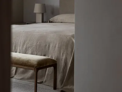 A minimalist bedroom featuring a bed with neutral-colored fabric bedding and a wooden bench.