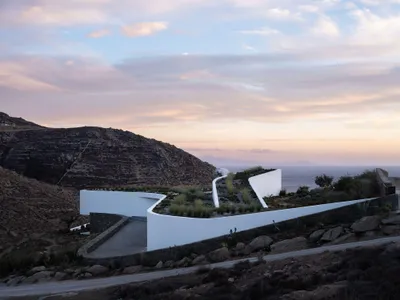 A minimalist cliffside resort hotel featuring white buildings with curved walls and steps leading down to the ocean.