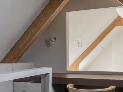 A modern home office features a concrete floor, wooden beams, and a metal desk.