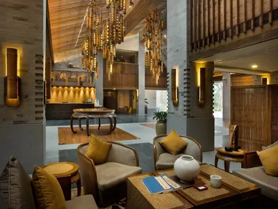 Spacious hotel lobby with wooden floors and furnishings, featuring tall ceilings with wooden slat ceiling and hanging chandel