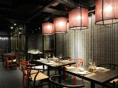 An industrial-style restaurant interior with wooden seating, fabric lighting fixtures, and metal elements.