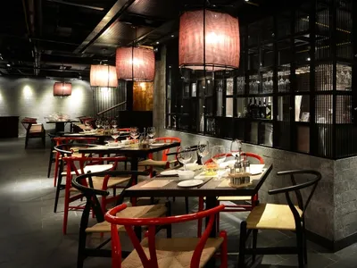 A contemporary dining room with red and black furniture, wooden chairs, and concrete walls.