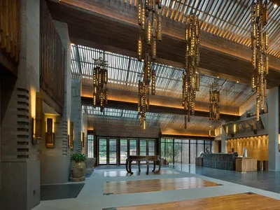 Modern hotel lobby with wooden flooring and ceiling, large windows, and hanging chandeliers.