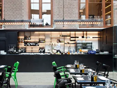 A modern restaurant interior featuring black and green accents, with a bar, tables, chairs, and a glass display case.
