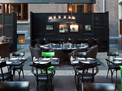 A modern restaurant interior featuring black metallic furniture adorned with green accents, including green chairs and green