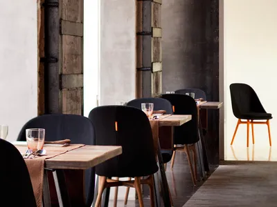 Industrial-style restaurant interior with wooden tables, concrete walls, and black chairs and accents.