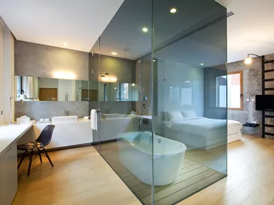 A modern minimalist bedroom featuring a glass-enclosed bathtub and a concrete wall.
