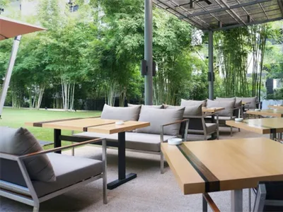 Modern outdoor restaurant patio with wooden tables and metal chairs surrounded by greenery and bamboo