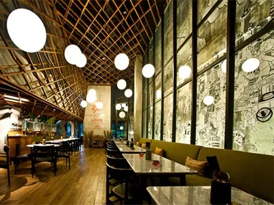 A spacious modern restaurant with industrial design elements including wooden beams, concrete walls, and large glass windows.