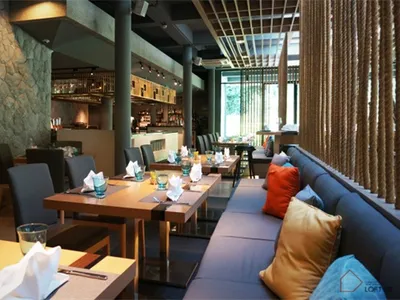 Modern restaurant interior with stone wall, wooden tables, and blue seating area.
