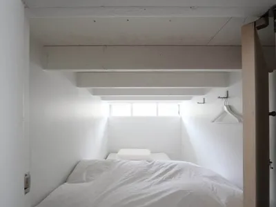 A minimalist bedroom with a bed covered in white textiles and a small window on the ceiling.