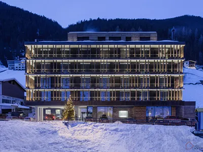 現代酒店建築搭配玻璃陽台與混凝土結構，在雪景中於黃昏時分被燈光照亮